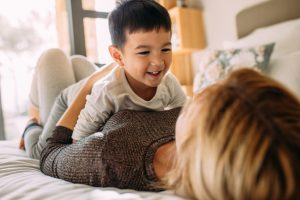 Cute little kid playing with his mother on bed. Mother and son having a fun time at home.